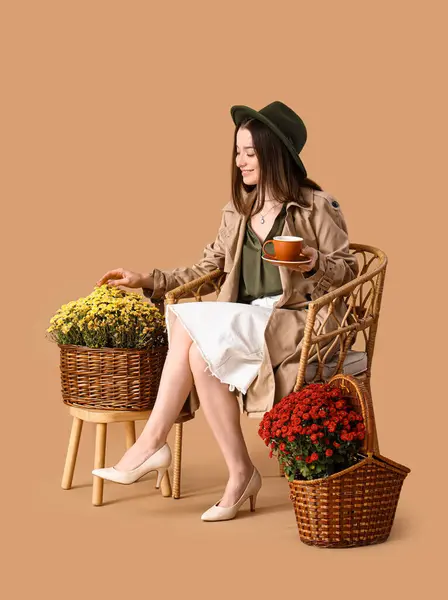 Junge Frau Mit Kaffeetasse Sessel Und Chrysanthemenblumen Auf Beigem Hintergrund — Stockfoto