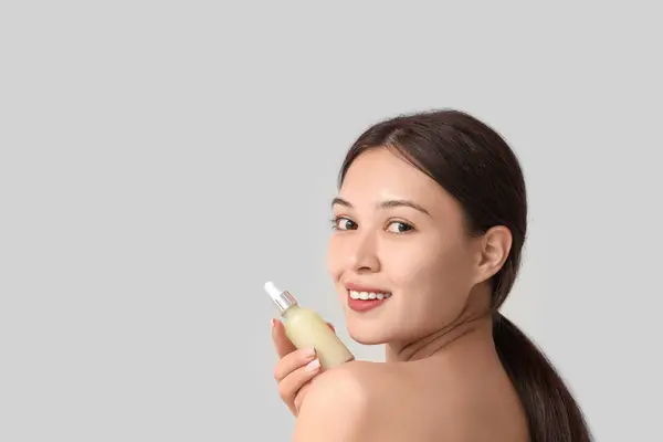 Gri Arka Planda Kozmetik Yağı Şişesiyle Güzel Bir Asyalı Kadın — Stok fotoğraf