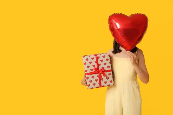 黄色の背景にギフトボックスとハート型の気球を持つ美しい若い女性 バレンタインデーのお祝い — ストック写真