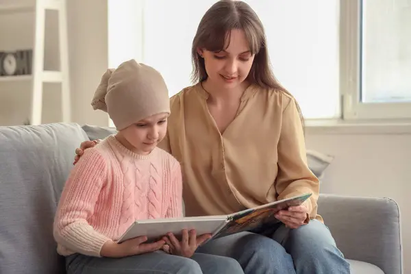 Little girl after chemotherapy with her mother reading book at home. International Childhood Cancer Day