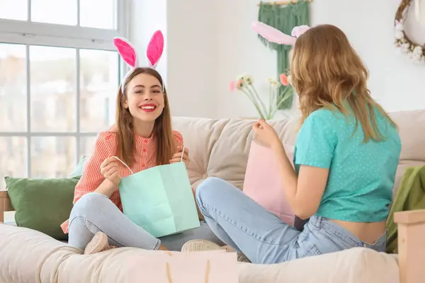 Happy young women in bunny ears headbands unpacking shopping bags for Easter at home