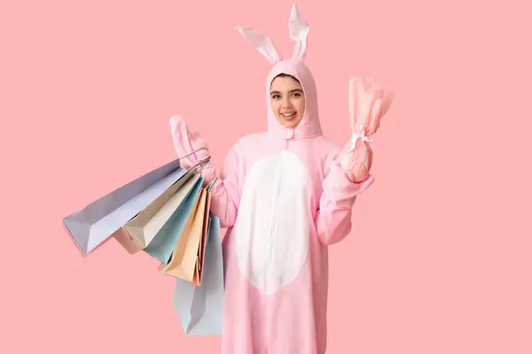 ピンクの背景にイースターギフトエッグとショッピングバッグとバニーコスチュームの美しい若い女性 — ストック写真