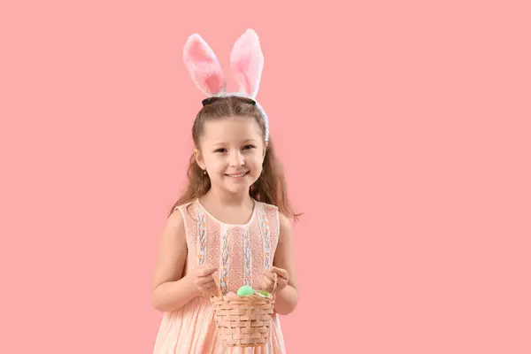 可爱的小女孩 长着小兔子耳朵 手里拿着柳条篮和粉色背景的复活节彩蛋 — 图库照片