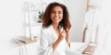 Genç Afro-Amerikalı kadın banyoda saç spreyi kullanıyor.