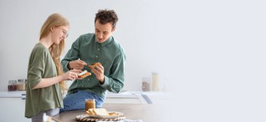 Genç kadın ve erkek mutfakta tost ekmeğine fındık ezmesi sürüyor. Tasarım için pankart