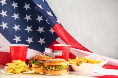 Lezzetli hamburgerler, patates cipsleri, nacho 'lar, bir bardak içecek ve arka planda Amerikan bayrağı. Anma Günü kutlaması
