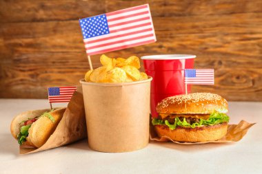 Lezzetli burger, patates cipsi, sosisli sandviç ve bir bardak içki, tahta arka planda. Anma Günü kutlaması