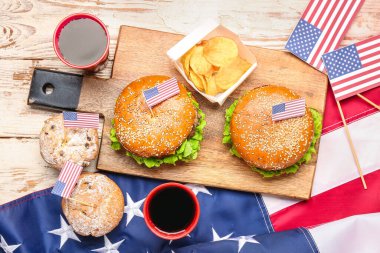 Lezzetli hamburgerler, patates cipsleri, kekler, kola ve hafif ahşap arka planda Amerikan bayrağı. Anma Günü kutlaması