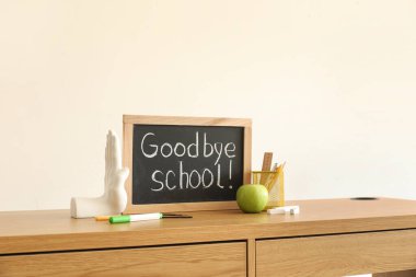Işık duvarının yanındaki masa üzerinde GOODBYE OKULU, elma ve kırtasiye yazı tahtası