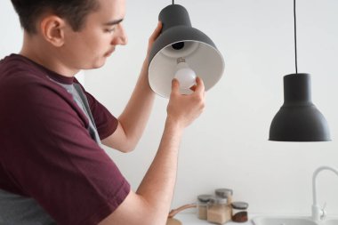 Genç adam mutfakta ampul değiştiriyor.