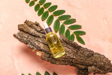 Ağaç kabuğu ve pembe arka planda yaprakları olan bir şişe kozmetik yağı.