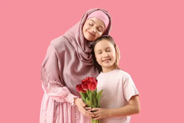 女の子とともにチューリップと彼女のイスラム教徒の母親上のピンクの背景 — ストック写真
