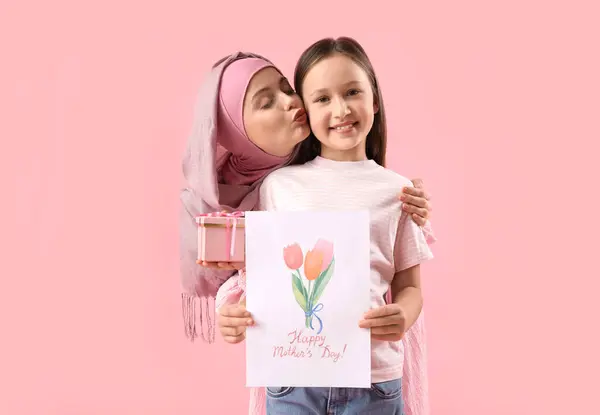 小さな女の子ともに挨拶カードとギフトのために彼女のイスラム教徒の母親上のピンクの背景 — ストック写真