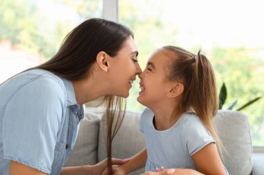 Mutlu anne ve kızı oturma odasında kanepede oturuyor ve burunlarına dokunuyor.