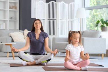 Küçük kızı oturma odasında yerde meditasyon yaparken mutlu bir anne.