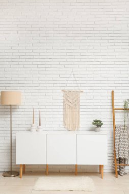 Odada beyaz tuğla duvarın yanında merdiveni ve lambası olan modern beyaz çekmeceler.