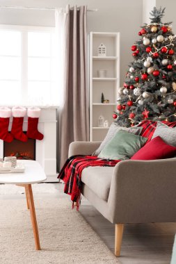 Oturma odasının içinde kanepe, Noel ağacı ve şömine var.