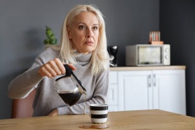 Depresyondaki olgun kadın mutfağa kahve dolduruyor.