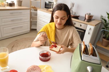 Genç, güzel, mutlu bir kadın mutfakta reçelli tost yapıyor.