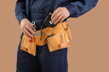 Kahverengi arka planda alet kemeriyle mezurası olan erkek inşaat işçisi, yakın plan.