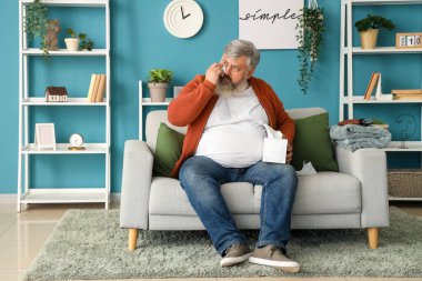 Oturma odasında peçeteyle gözlerini silen üzgün yaşlı adamın portresi.