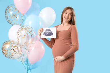 Sonogram görüntüsü olan hamile bir kadın ve mavi arka planda bebek partisi için balonlar.