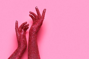 Pembe arka planda parıltıyla kaplı kadın elleri, yakın plan.