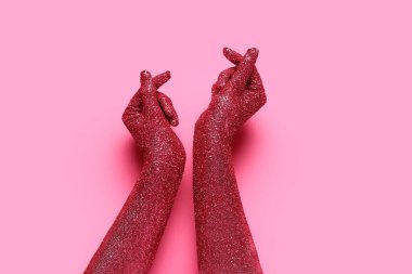 Elleri boyalı bir kadın pembe arka planda kalp yapıyor, yakın plan.