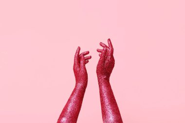 Pembe arka planda parıltıyla kaplı kadın elleri, yakın plan.