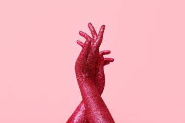 Pembe arka planda parıltıyla kaplı kadın elleri, yakın plan.