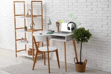 Beyaz duvarın yanında işyeri, ev bitkisi ve raf ünitesi olan modern bir oda.