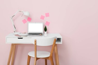 Lambalı, dizüstü bilgisayarlı ve pembe duvarlı güzel bir iş yeri.