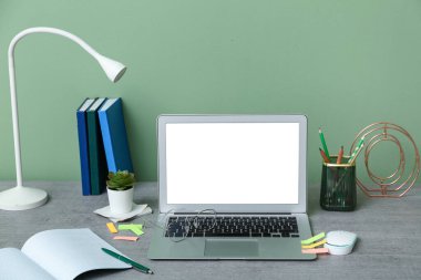 Yeşil duvarın yanında dizüstü bilgisayarı, kırtasiyesi ve lambası olan modern ofis çalışma alanı