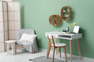 Çalışma odası, ev bitkisi, koltuk ve rafları yeşil duvarın yanında olan şık bir oda.