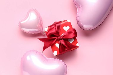 Pembe arka planda kalp şeklinde balonlar olan güzel bir hediye kutusu. Sevgililer Günü kutlaması