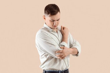 Bej arka planda kol ağrısı çeken genç bir adam.