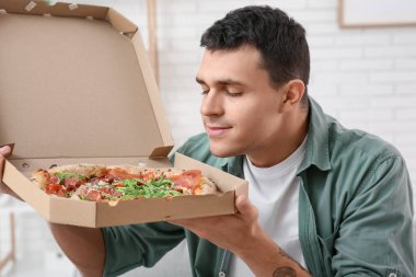 Genç adam elinde karton kutuyla lezzetli bir pizza tutuyor.