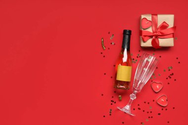 İçinde şampanya, cam, hediye kutusu ve kırmızı arka planda mumlar olan kompozisyon. Sevgililer Günü kutlaması