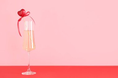 Masada pembe arka planda dekoru olan bir kadeh şampanya. Sevgililer Günü kutlaması