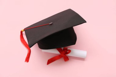 Mezuniyet şapkası ve pembe arka plan diploması.