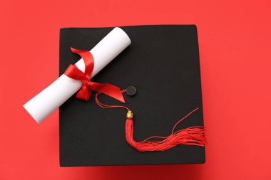 Kırmızı arka planda mezuniyet şapkası ve diploması.