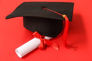 Kırmızı arka planda mezuniyet şapkası ve diploması.