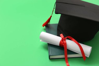 Diplomalı mezuniyet şapkası ve yeşil arka planda not defteri.