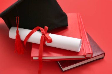 Diplomalı mezuniyet şapkası ve kırmızı zemin üzerine not defterleri.