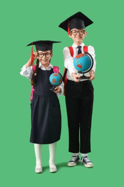 Yeşil arka planda küreleri olan mezuniyet şapkalı küçük çocuklar. Okul yılı sonu.