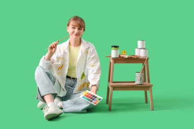 Yeşil arka planda oturan fırçalı ve boyalı kadın sanatçı