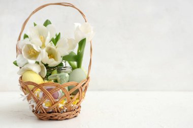 Dekoratif kozmetik ürünleri, Paskalya yumurtaları ve beyaz arka planda bir buket çiçekle dolu bir sepet.