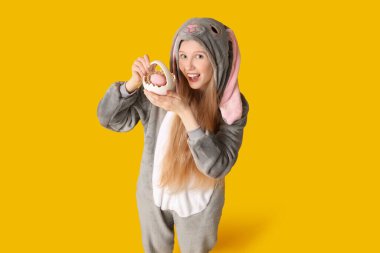 Tavşan kostümlü güzel genç bir kadın elinde sarı arka planda yumurta dolu bir sepet tutuyor. Paskalya kutlaması