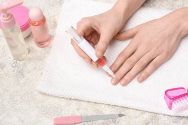 Havlu, kozmetik ürünler ve gri grunge arka planda manikür aletleri ile tırnak içi yağı kalemi tutan kadın eller.