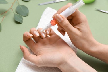 Yeşil arka planda tırnaklarına tırnak yağı süren kadın eller, yakın plan.